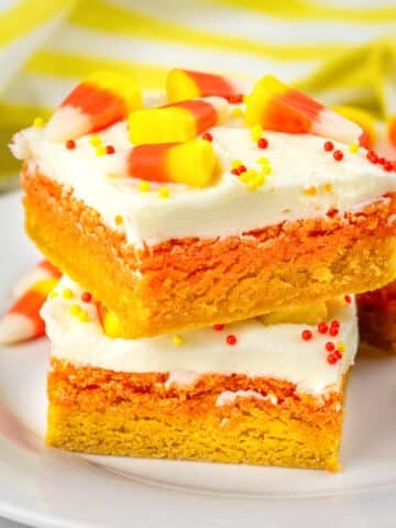 stack of two orange and yellow layered sugar cookie bars with white frosting and topped with candy corn and sprinkles.