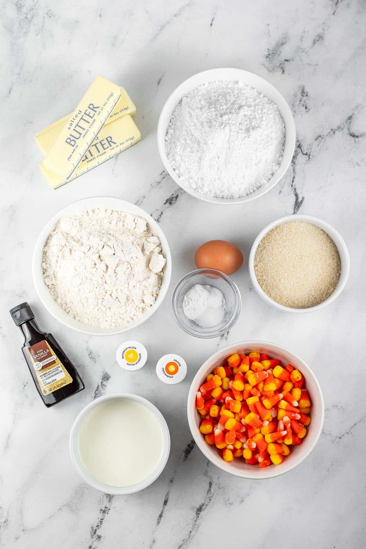 several white bowls with ingredients for sugar cookie bars - flour, butter, sugar, powdered sugar, vanilla extract, egg, baking powder, salt and candy corn.