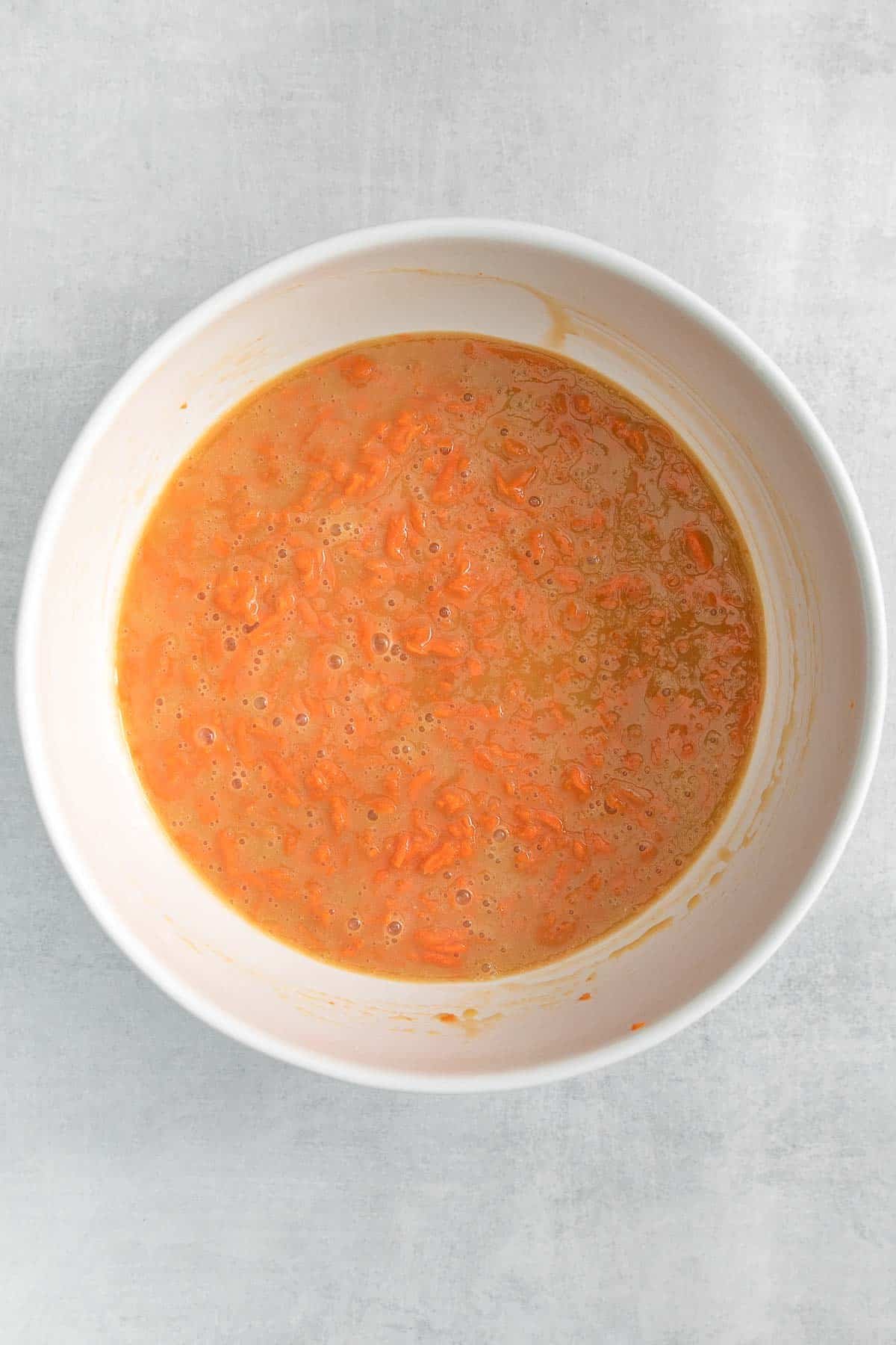 white mixing bowl with grated carrots in sugar and eggs mixture.