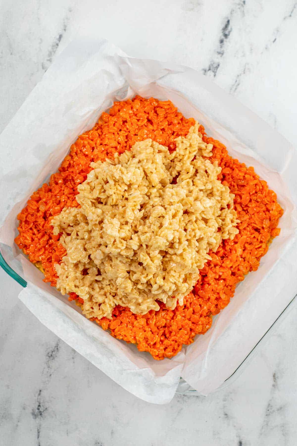 square glass dish with orange rice krispie treats topped white rice cereal mixture