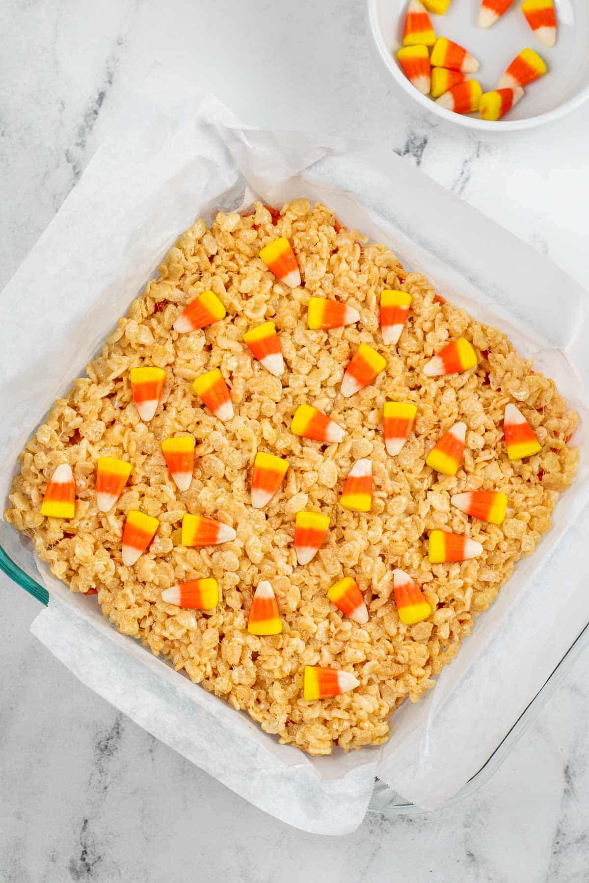 square glass dish with rice krispie treats topped with candy corn pieces.
