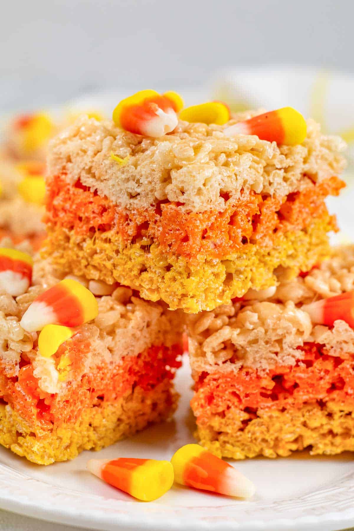 a stack of three yellow, orange and white layered rice krispie treats with candy corn on top