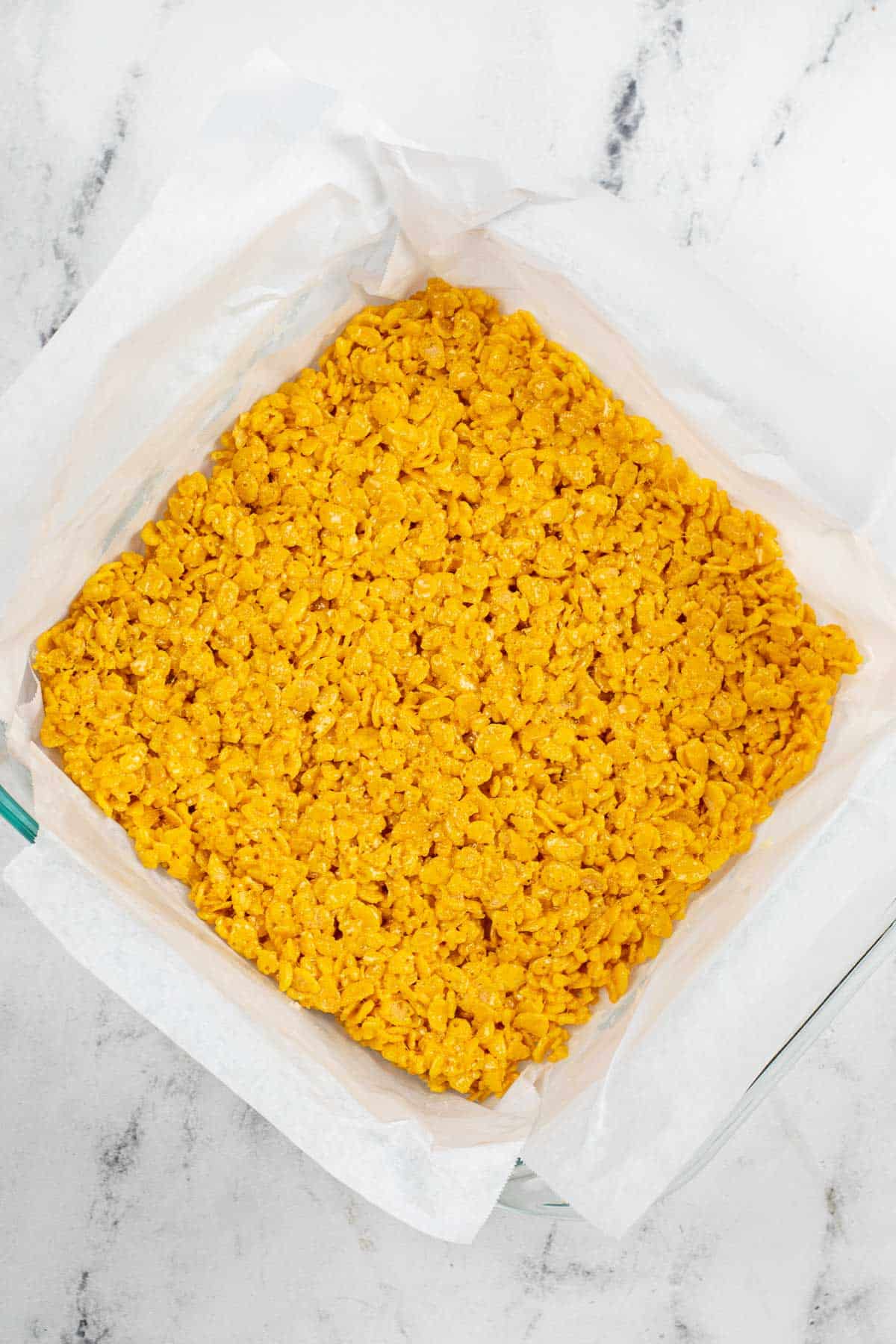 square glass dish with yellow colored rice krispie treats pressed down.