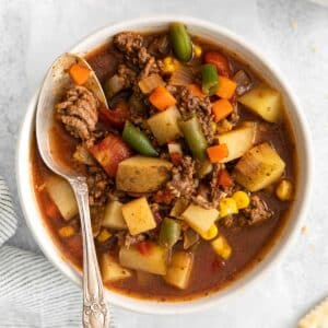 closeup of a white bowl of hamburger soup with potatoes and vegetables in a tomato broth.