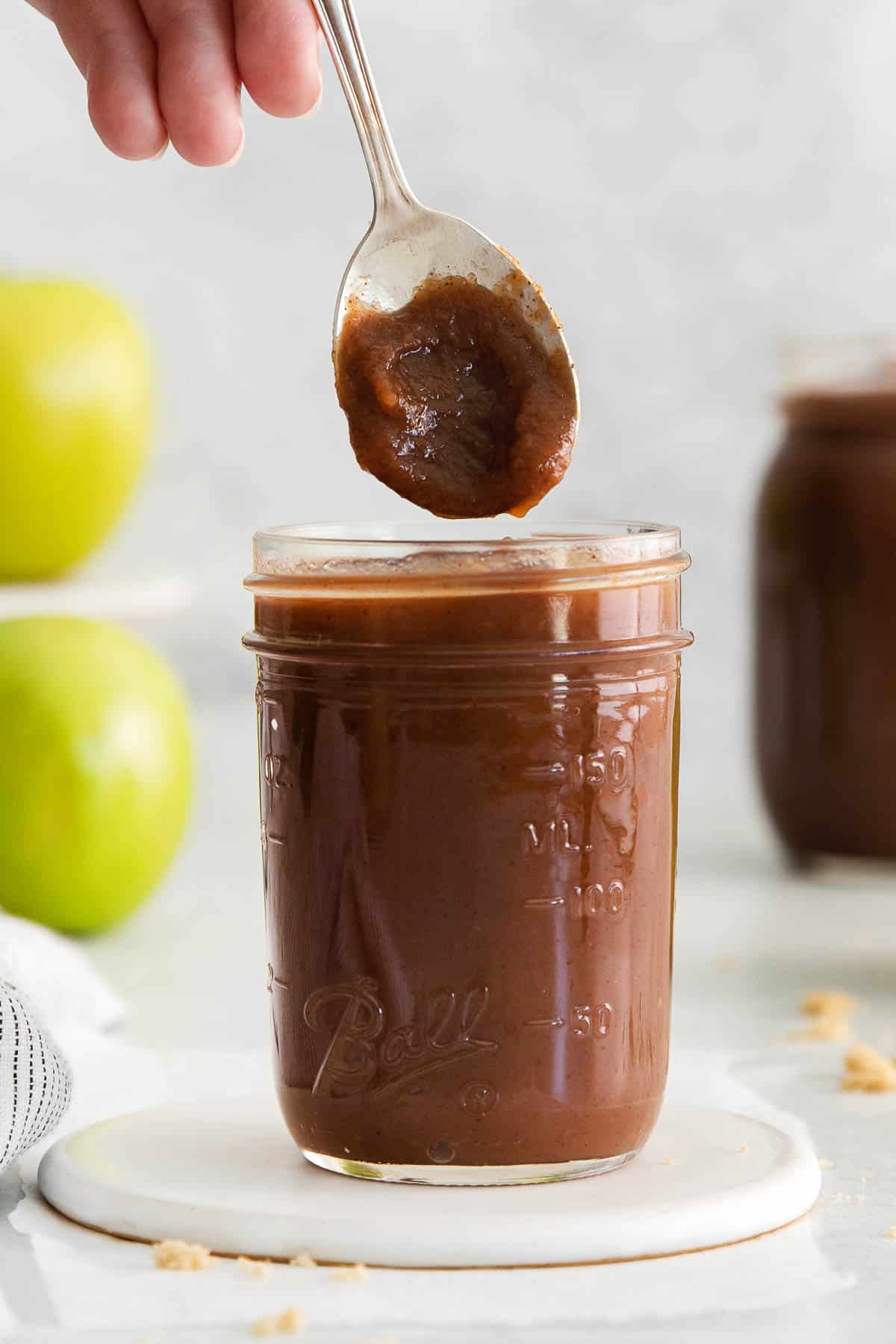 spoonful of apple butter over top of a jar of homemade apple butter on a white trivet.