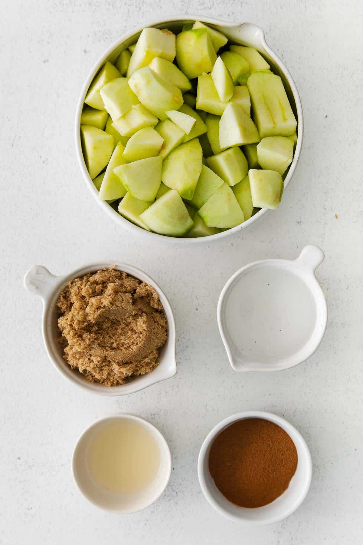 several white bowls with ingredients for apple butter - diced granny smith apples, brown sugar, cinnamon, lemon juice and water.