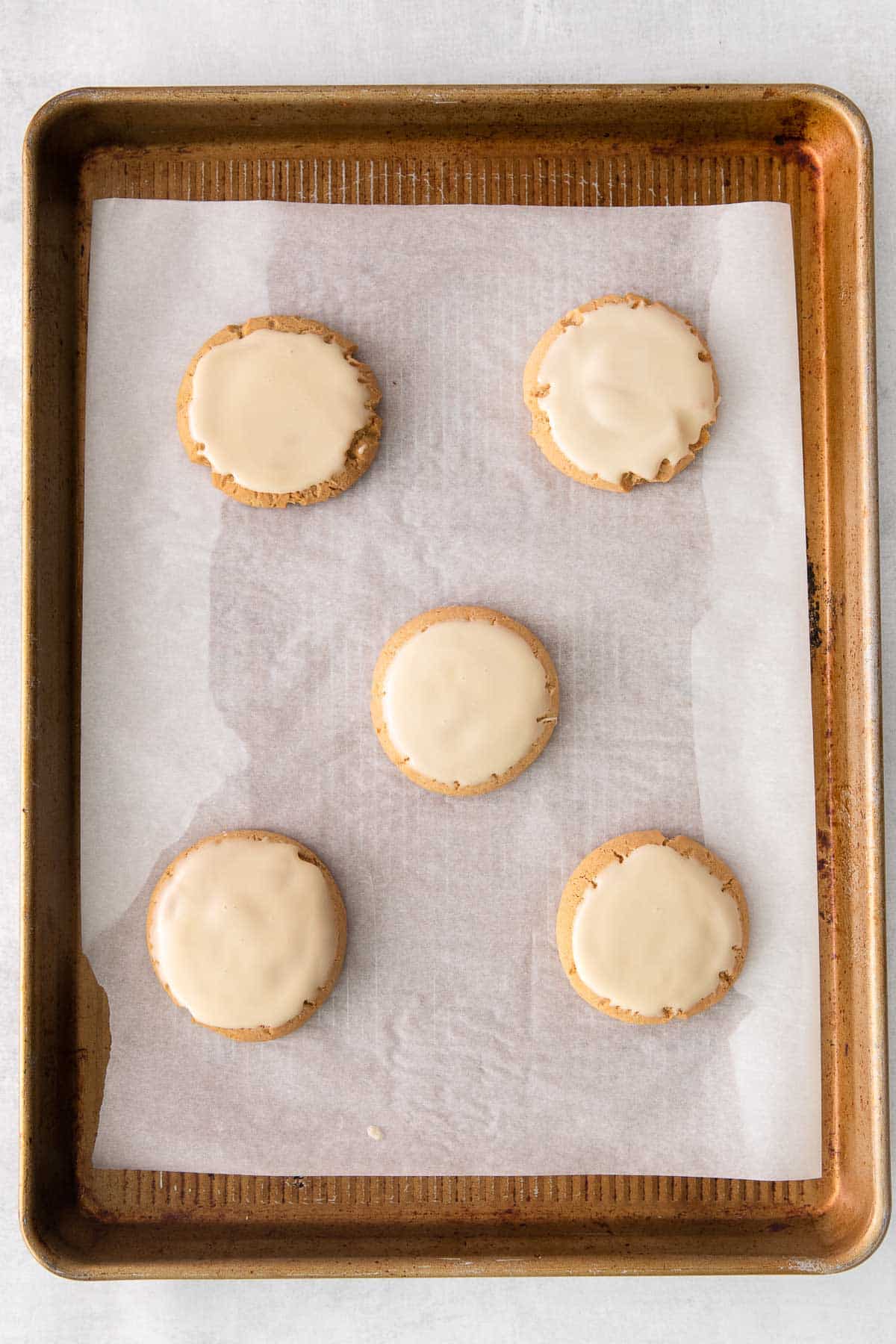 five maple brown sugar cookies with maple glaze on a baking sheet lined with parchment paper.