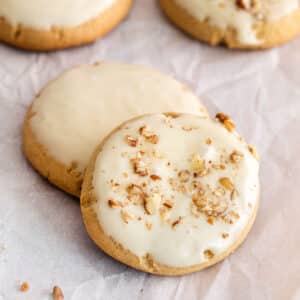 two maple brown sugar cookies topped with chopped nuts on white parchment paper