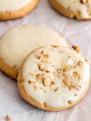 two maple brown sugar cookies topped with chopped nuts on white parchment paper