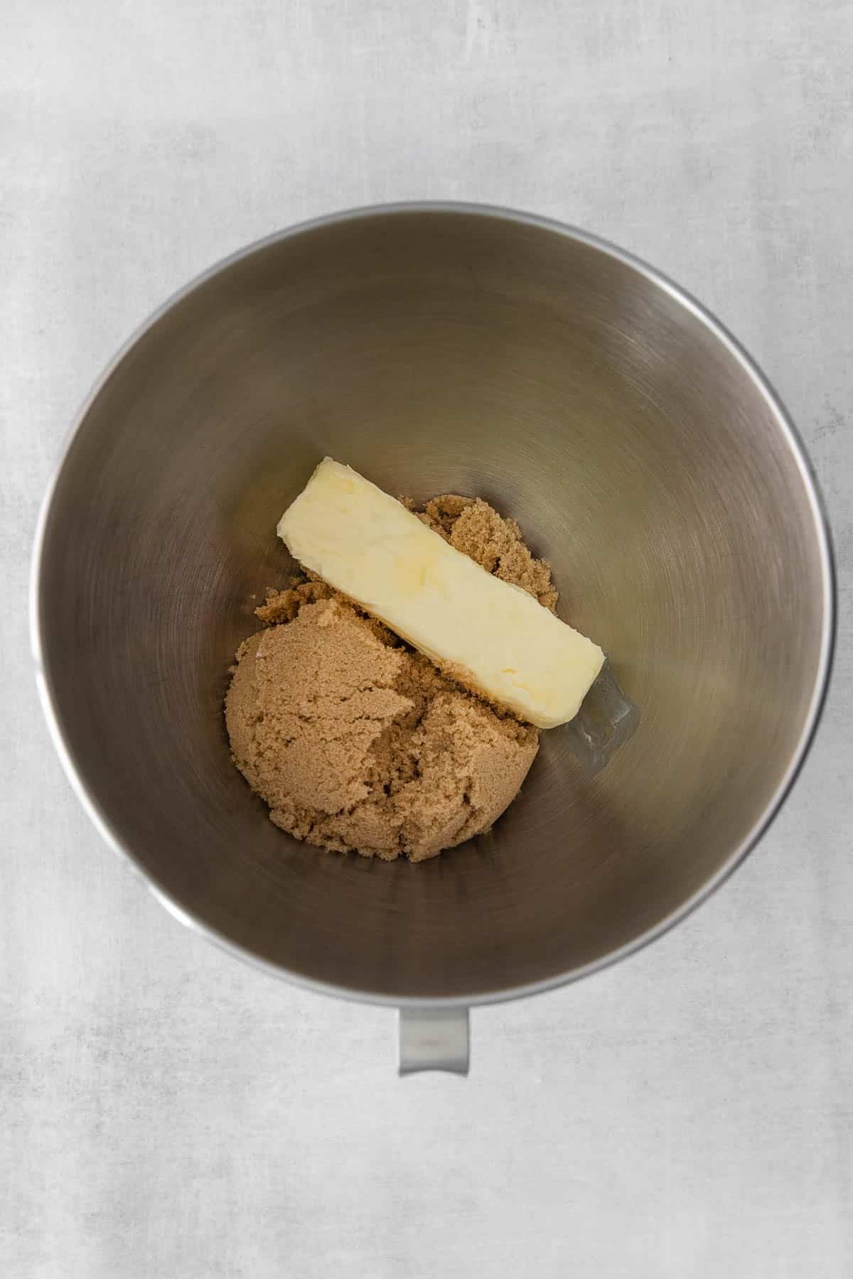 silver mixing bowl with brown sugar and a stick of butter.