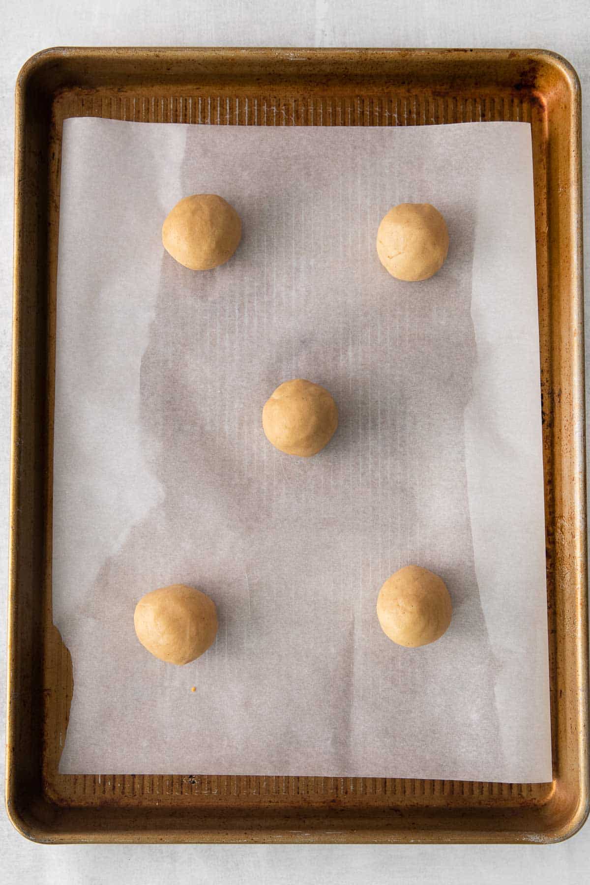 baking sheet lined with white parchment paper with 5 cookie dough balls.