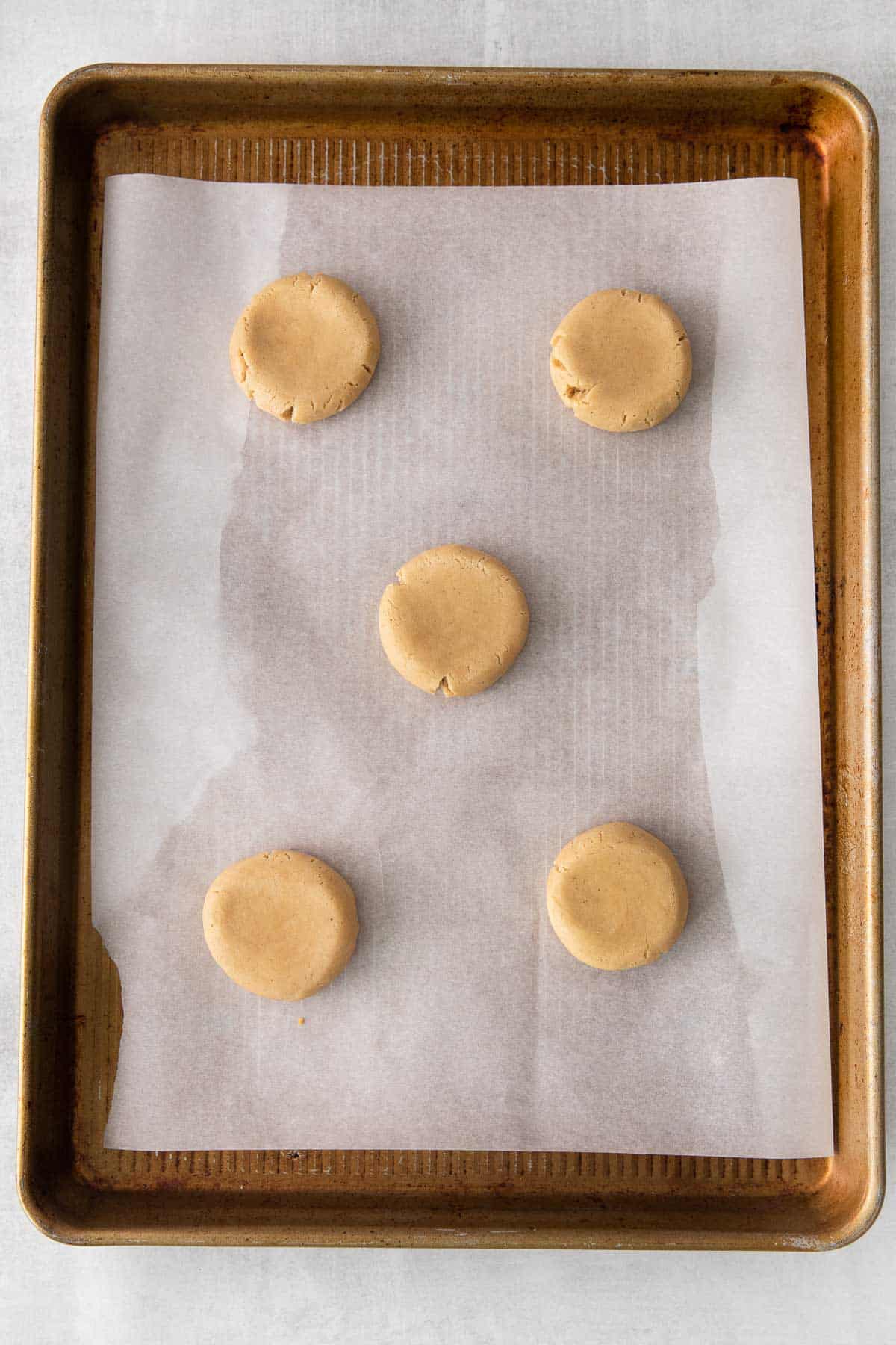 five raw cookies on a white parchment lined bakiing sheet.