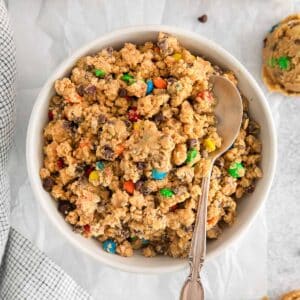 closeup of a bowl full of edible cookie dough with m&m's and chocolate chips mixed in.