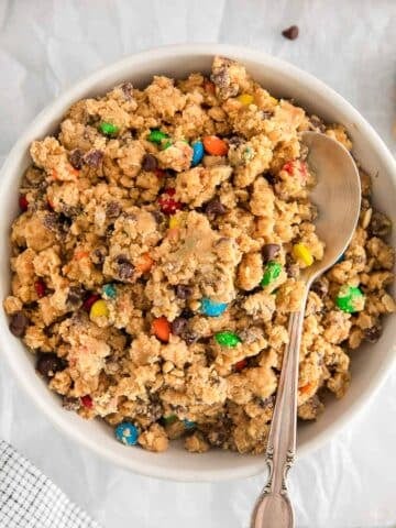 closeup of a bowl full of edible cookie dough with m&m's and chocolate chips mixed in.
