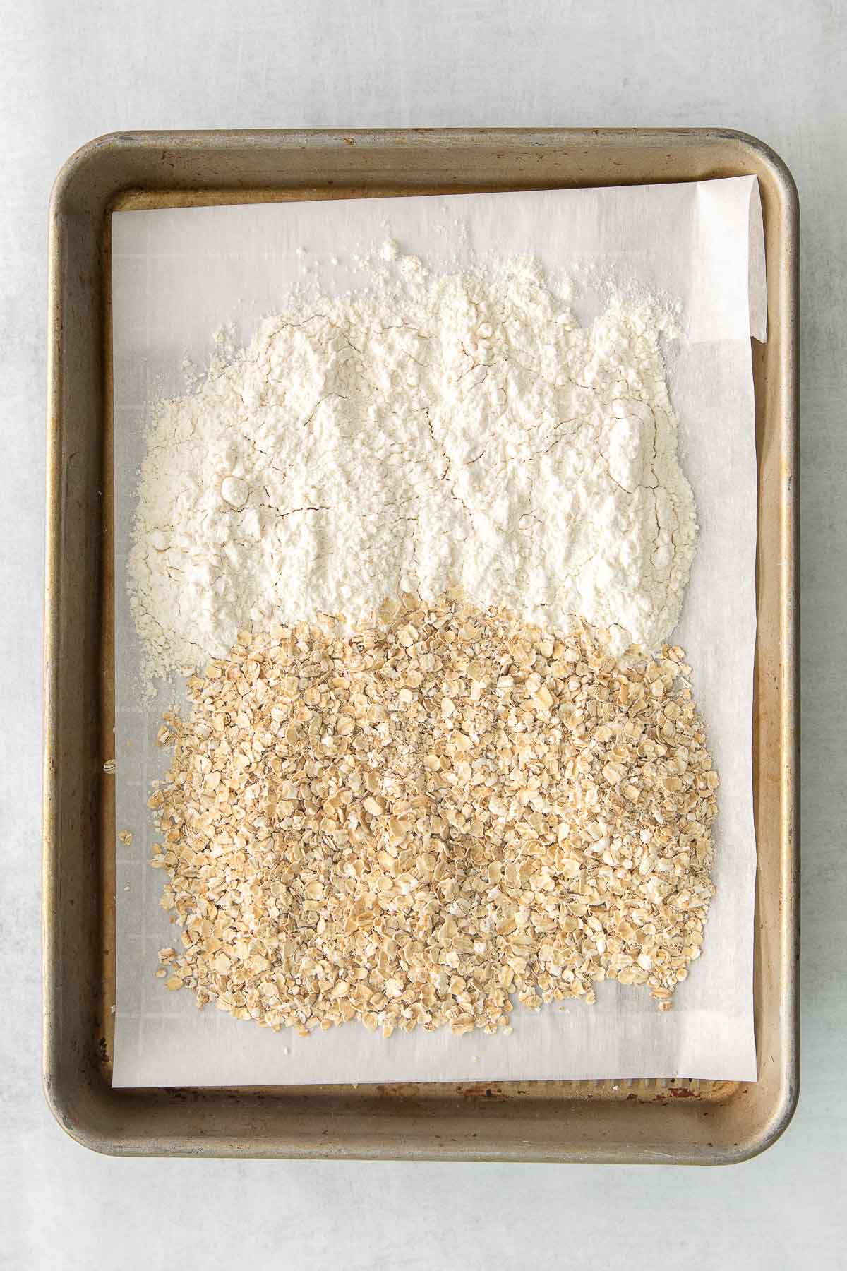 old fashioned oats and flour on a baking sheet lined with white parchment paper