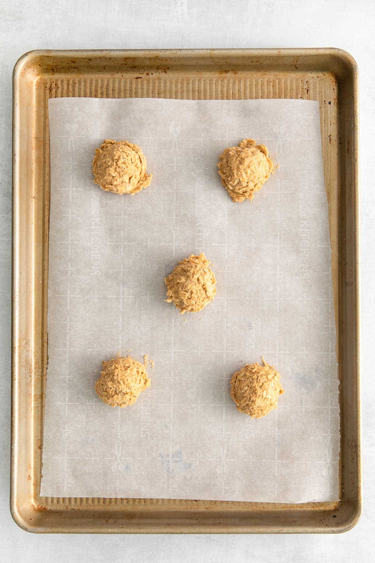 five pumpkin oatmeal cookie dough balls on a parchment lined baking sheet.