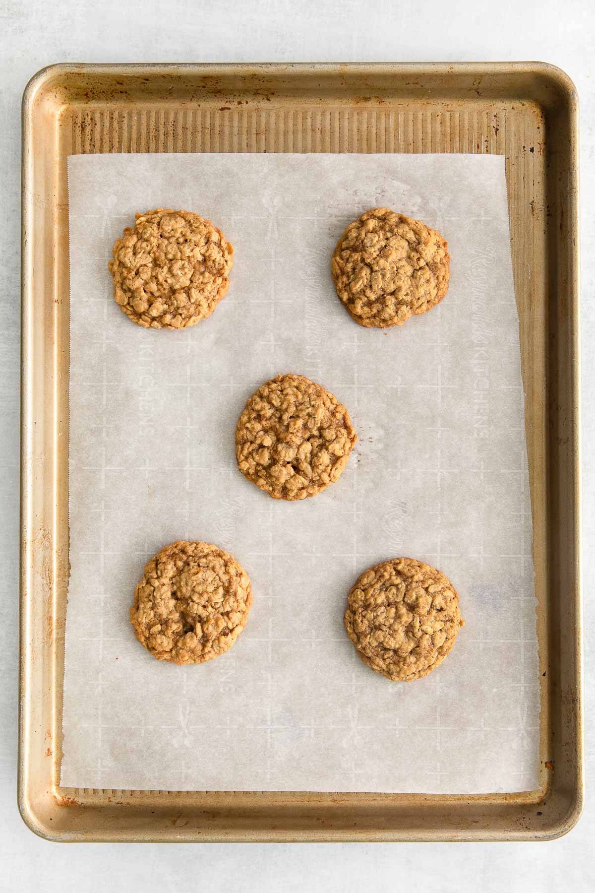 five baked oatmeal cookies on a white parchment paper lined cookie sheet.