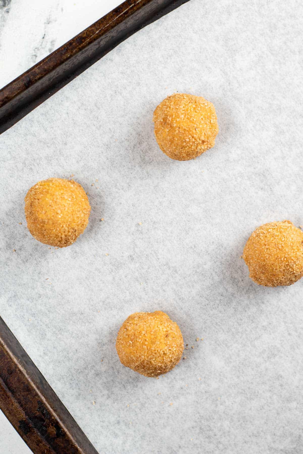 sugar coated pumpkin snickerdoodle dough balls on a baking sheet lined with white parchment paper.