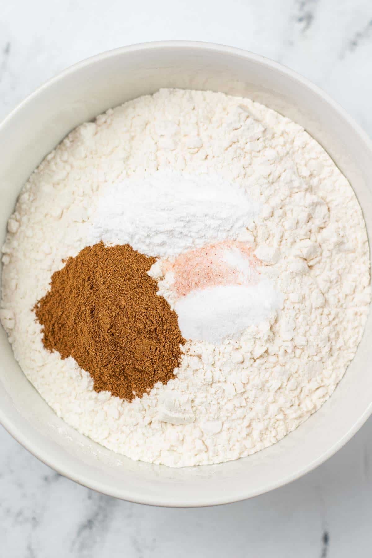white mixing bowl with flour, baking powder, cinnamon and salt on top.