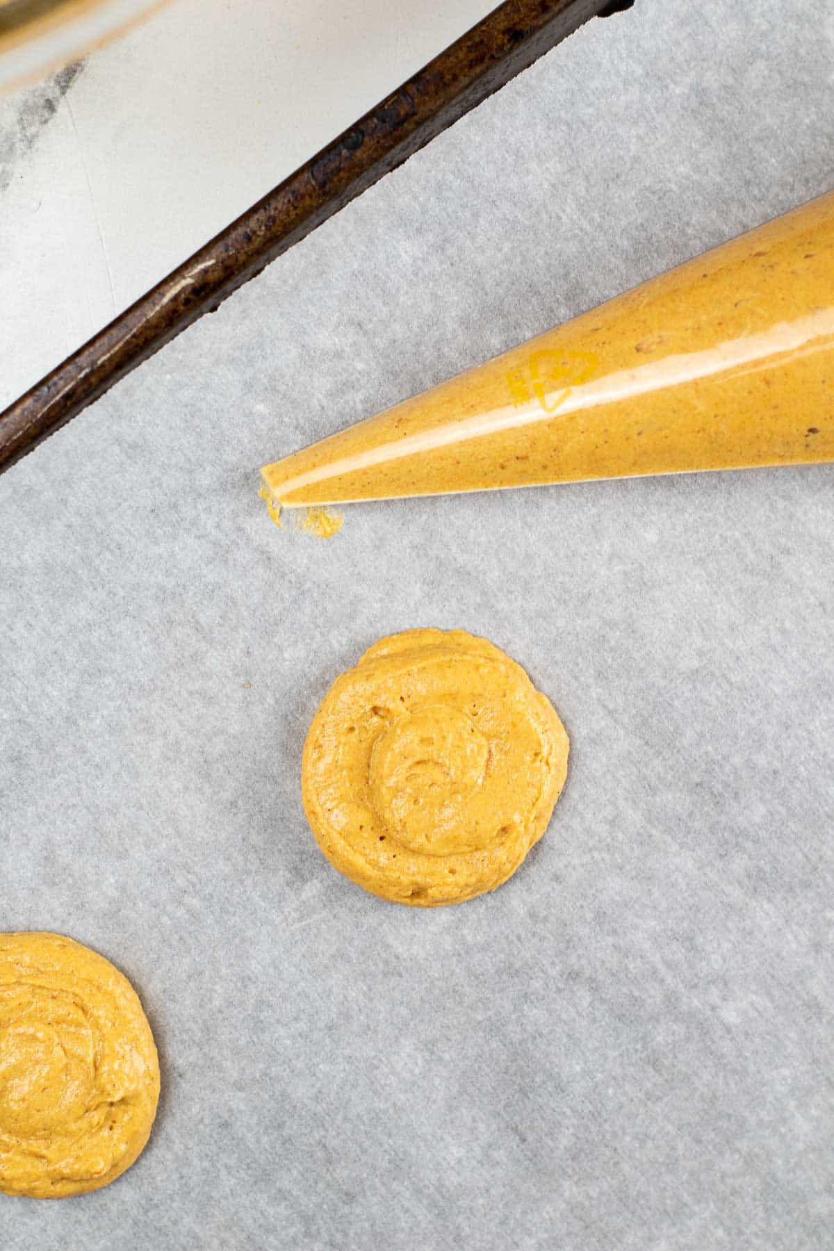 pumpkin cookie batter piped onto white parchment paper.