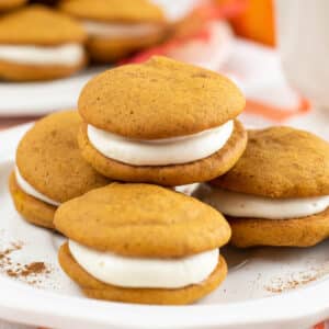 closeup of four pumpkin whoopie pies on a white plate.