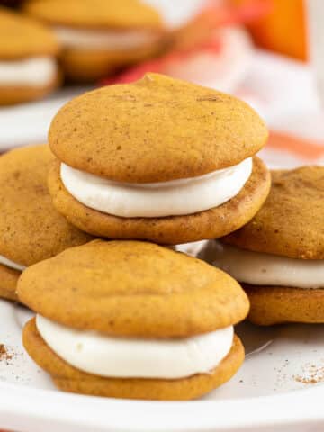 closeup of four pumpkin whoopie pies on a white plate.