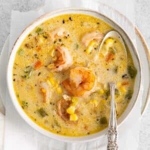 closeup of shrimp corn chowder in a white bowl with spoon in it.