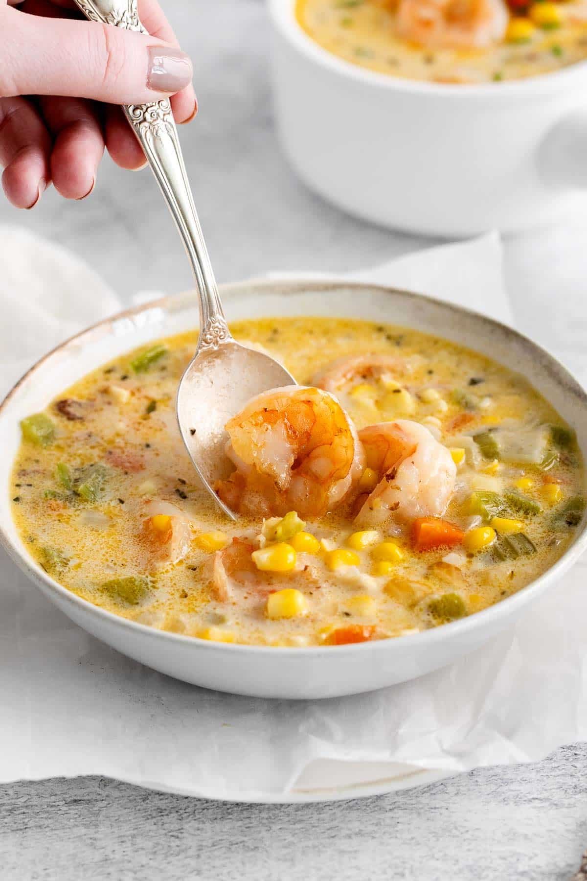 spoon dipping into shrimp corn chowder in a white bowl