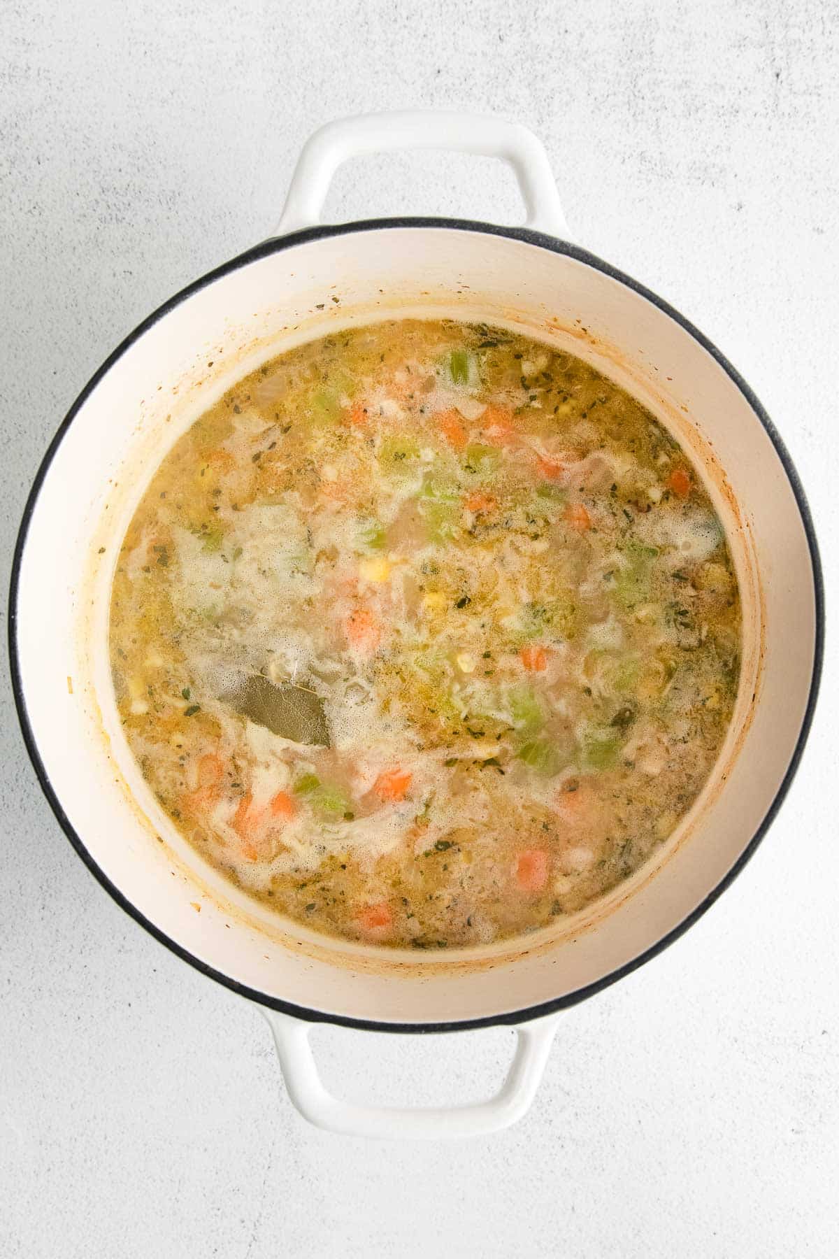 white dutch oven with broth, carrots and celery