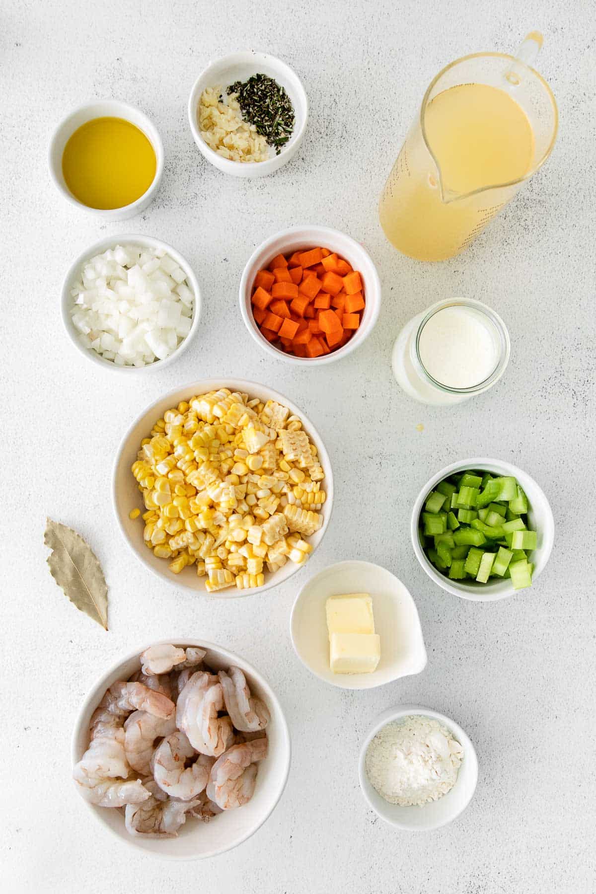 several white bowls with ingredients for shrimp and corn chowder - raw shrimp, flour, butter, cream, corn, celery, carrots, spices, broth