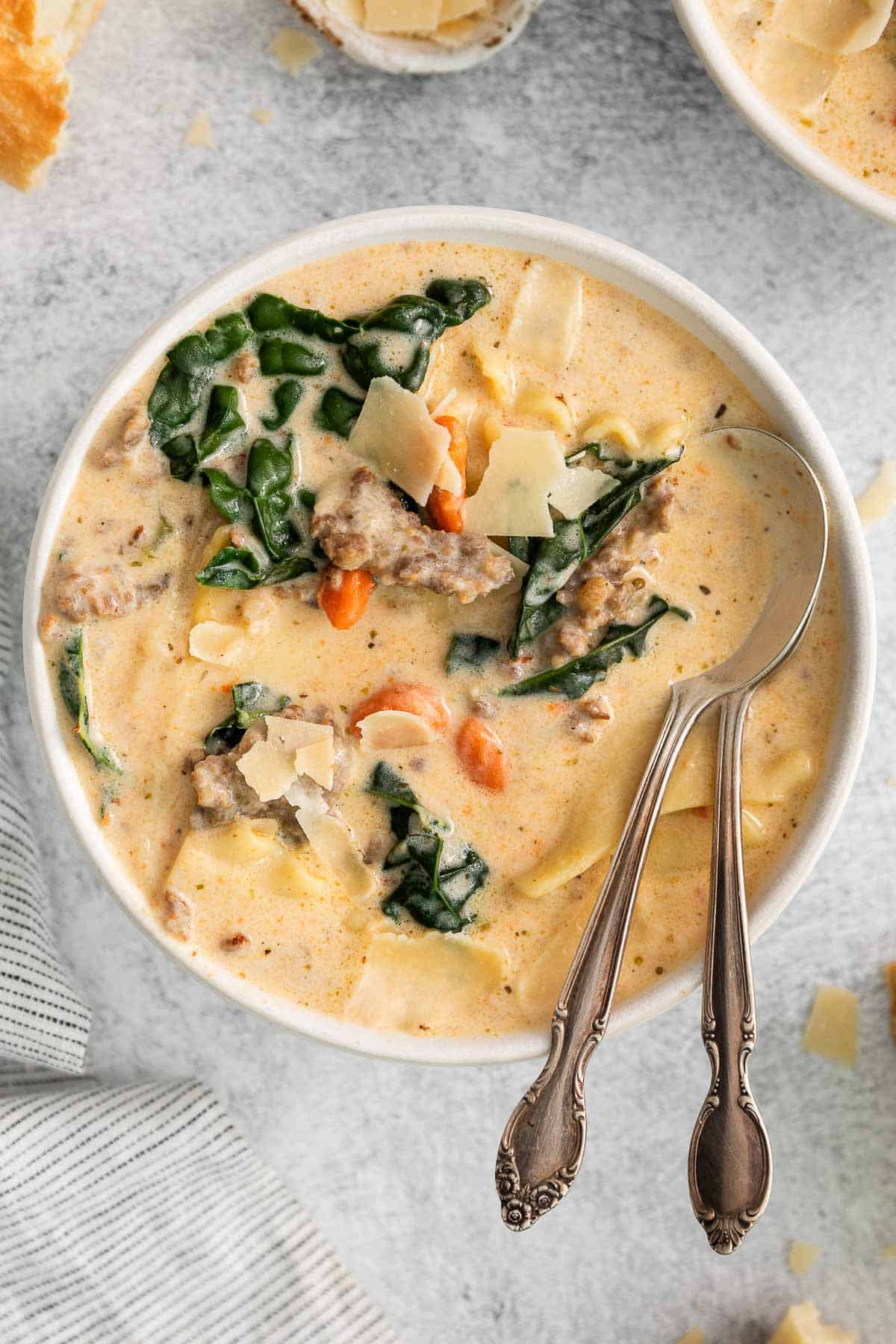 closeup of a white bowl of creamy white lasagna soup with kale and carrots and two spoons leaning on the side.