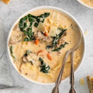 closeup of a bowl of creamy lasagna soup with ground meat and kale topped with shaved parmesan cheese