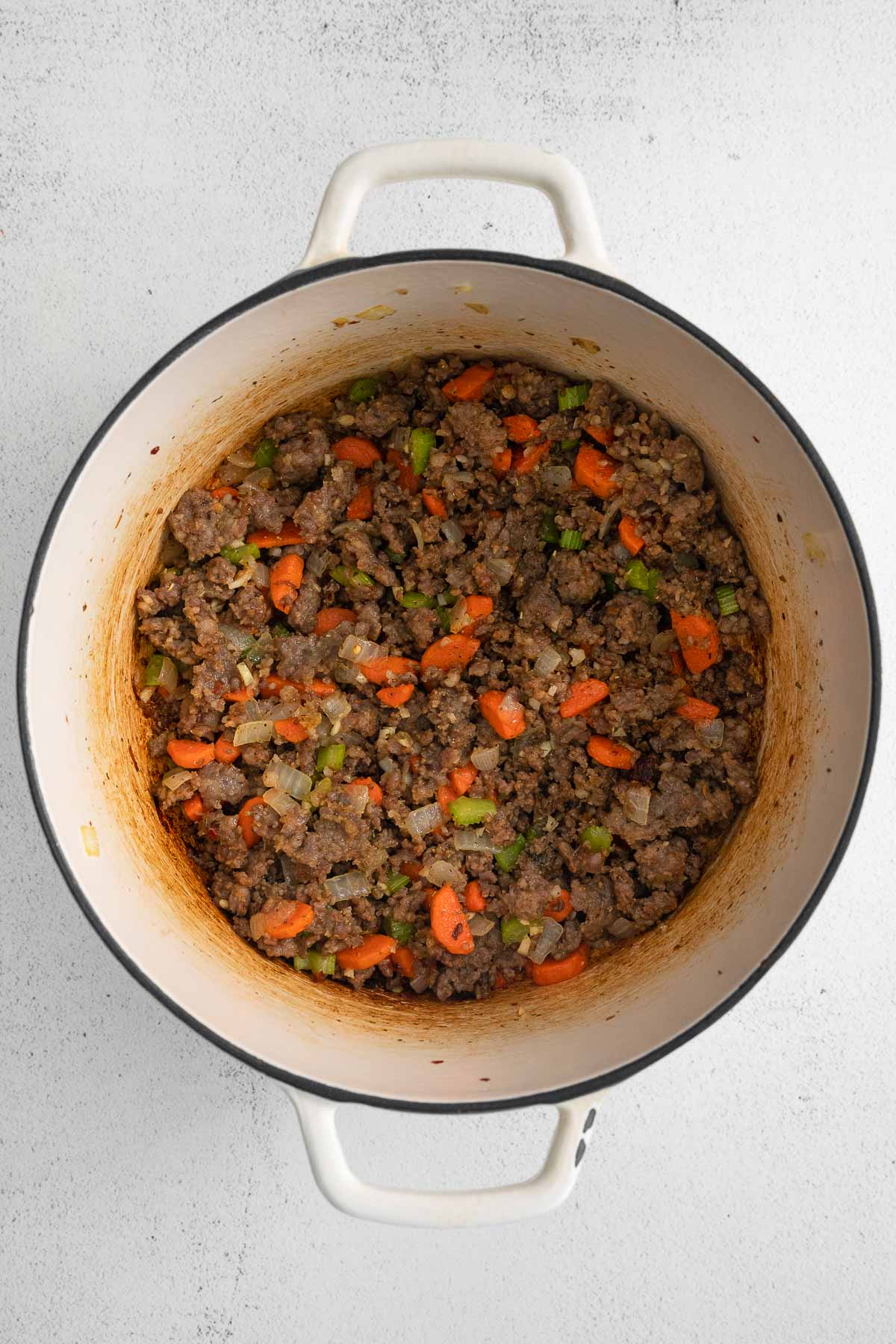 white pot with ground sausage with diced carrot, celery and onions.
