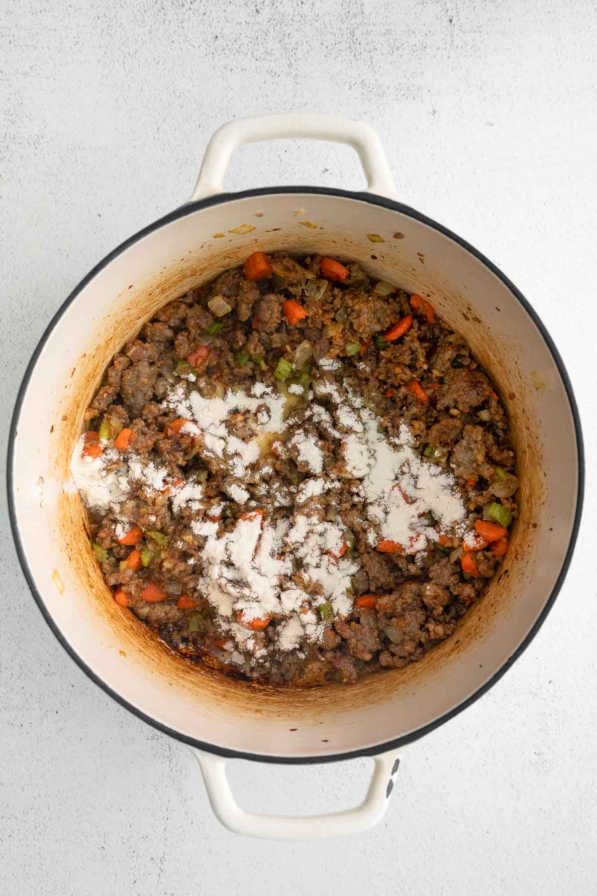 white pot with ground meat with flour sprinkled on top.