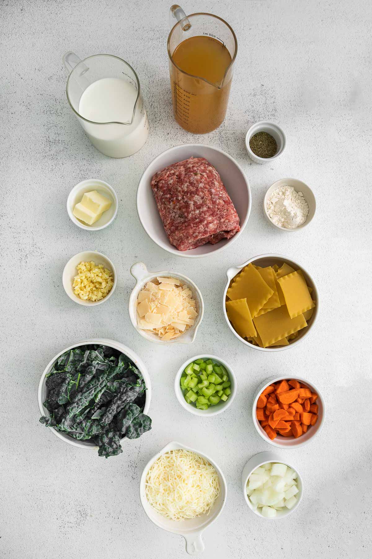 several bowls with ingredients for white lasagna soup - noodles, ground sausage, cream , kale, carrots, celery, onions, broth and parmesan cheese.