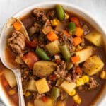 white bowl full of hamburger vegetable soup with potatoes in a tomato broth.