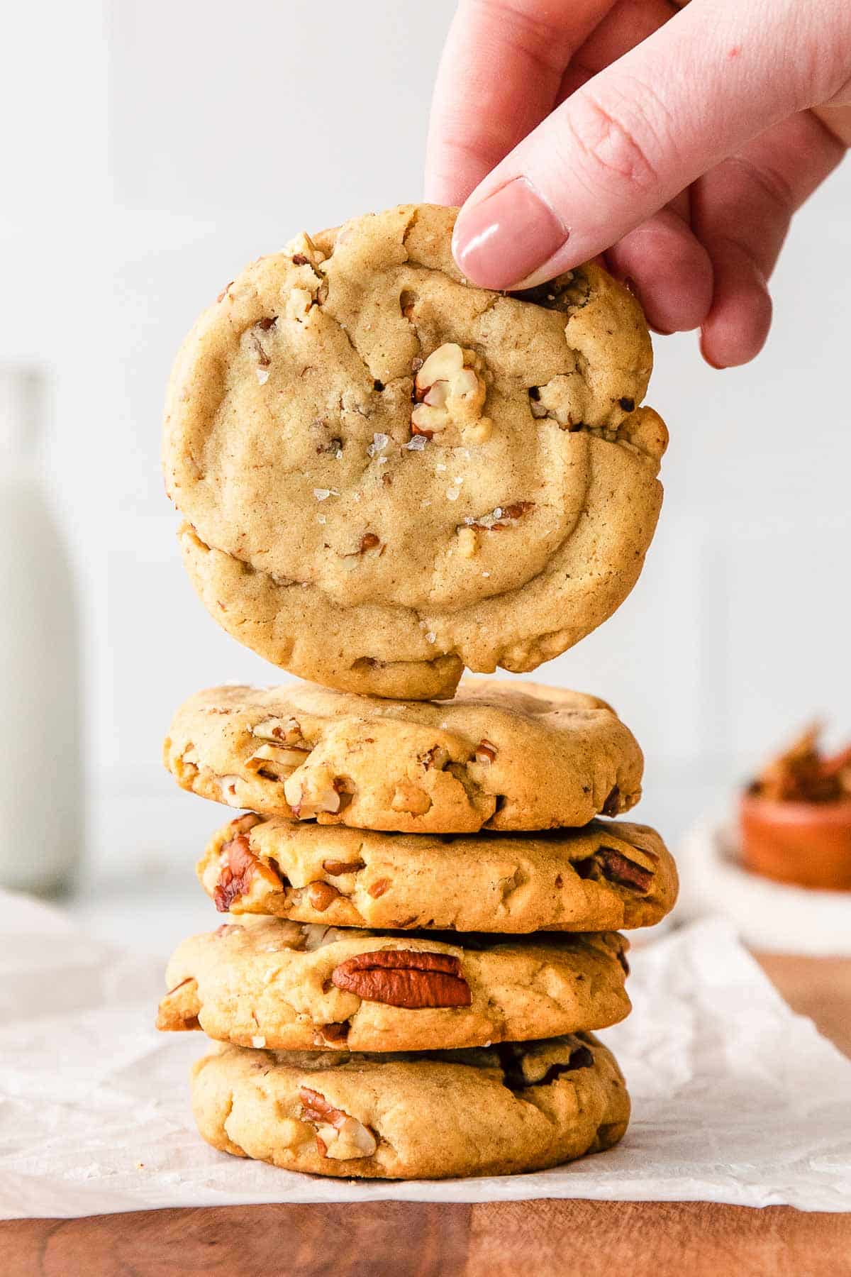 a woman's finger holding a butter pecan cookie over a stack of four cookies.