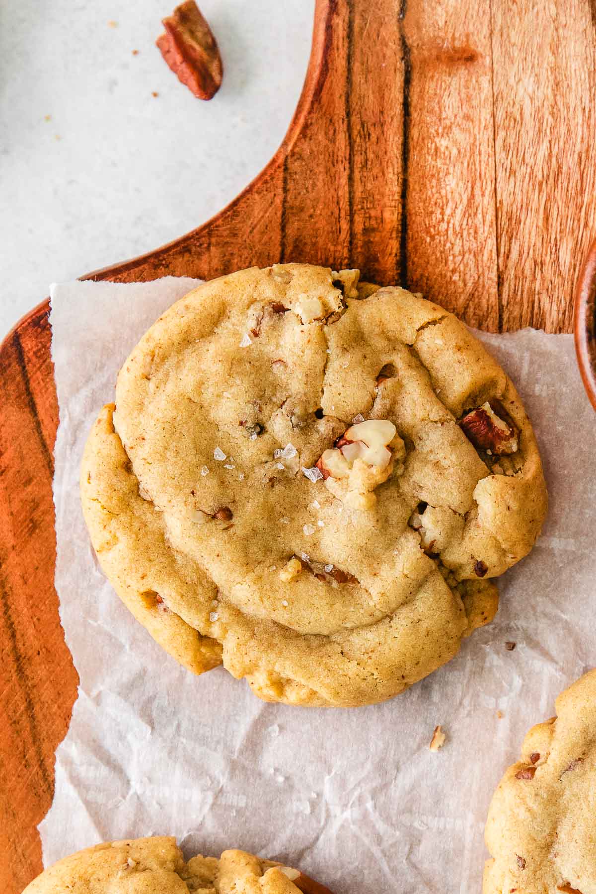 closeup of a butter pecan cookie on white parchment paper.