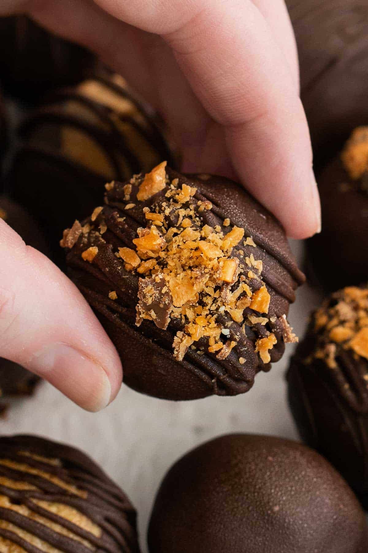closeup of a woman's fingers holding a chocolate covered butterfinger ball coated with crushed butterfingers.
