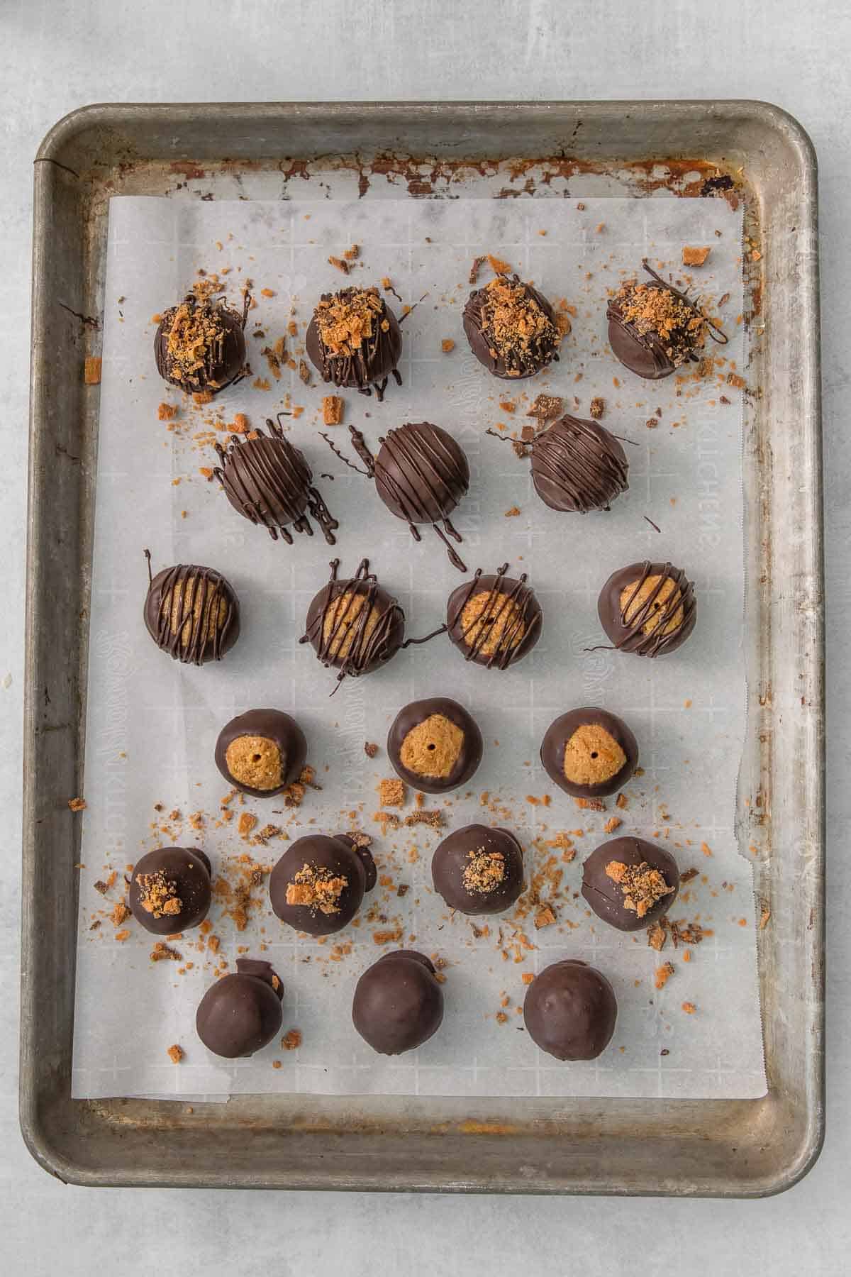 a baking sheet full of chocolate covered butterfinger peanut butter balls topped with crushed butterfingers.