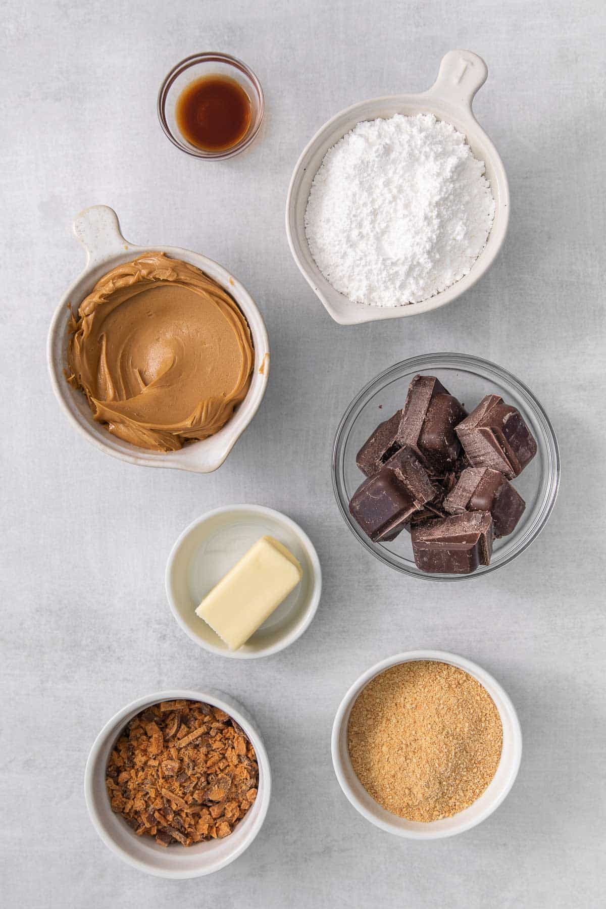 several bowls with ingredients for butterfinger balls - peanut butter, powdered sugar, crushed graham crackers, chocolate bark, vanilla extract and butter.
