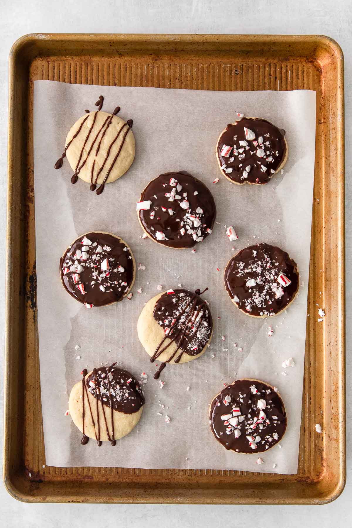eight shortbread cookies dipped in chocolate and topped with crushed peppermint candy on a baking sheet.
