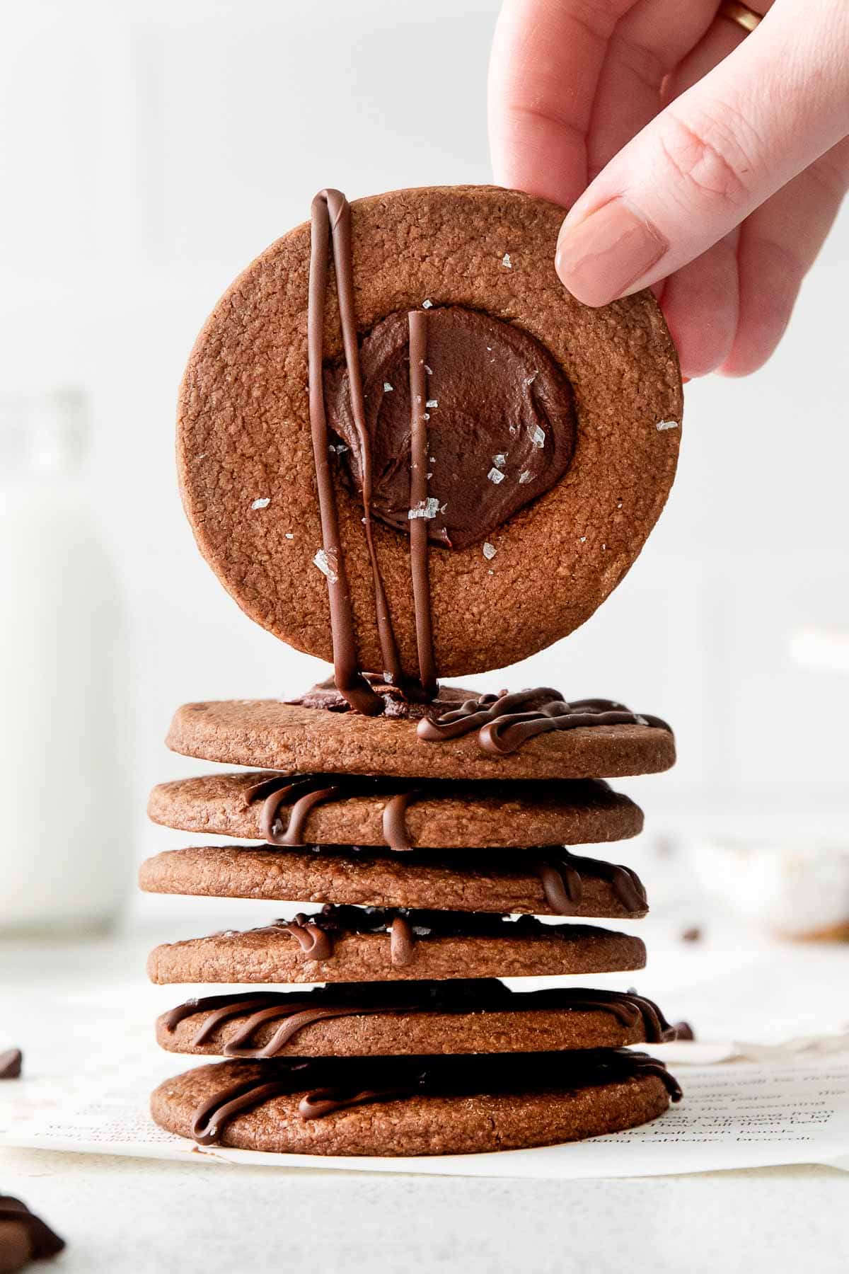 a stack of six chocolate cookies with a woman's hand holding one of them over the top of the stack.