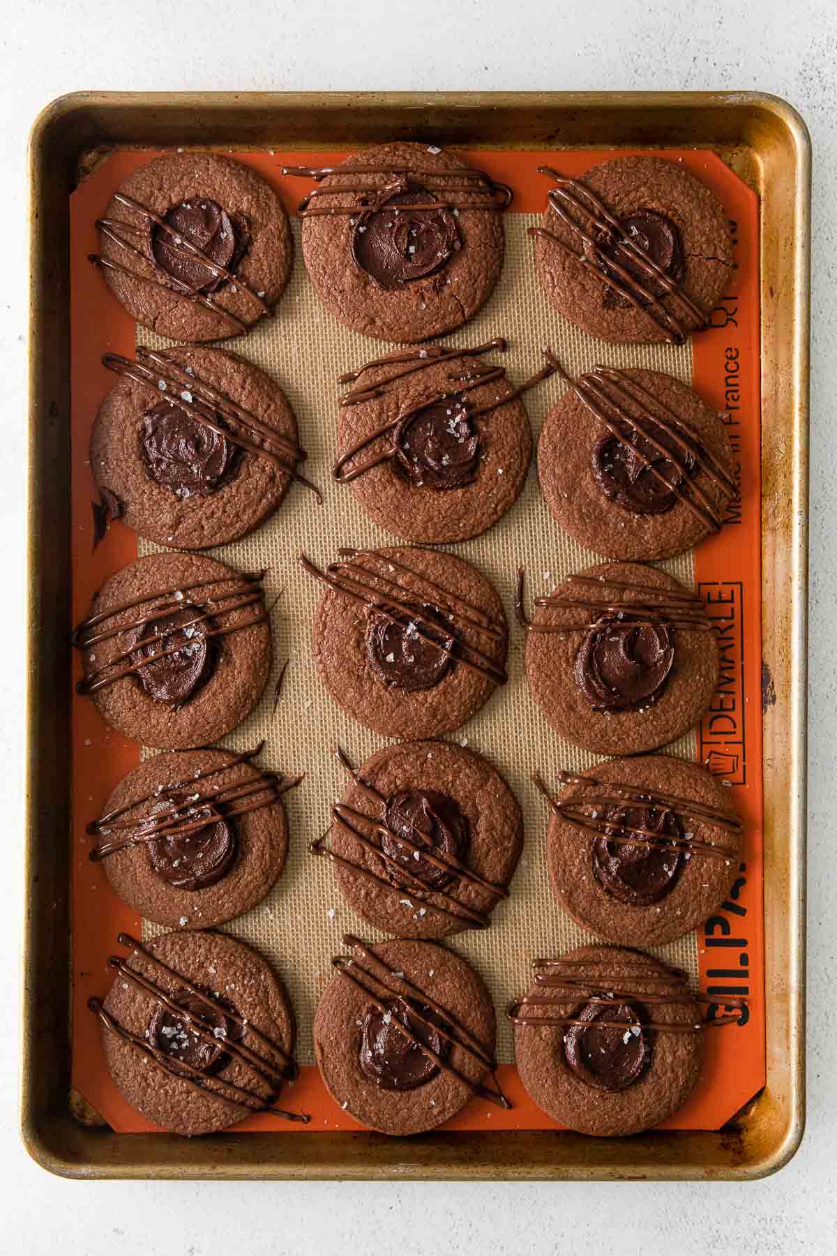 fifteen double chocolate thumbprint cookies with chocolate filling on a baking sheet.