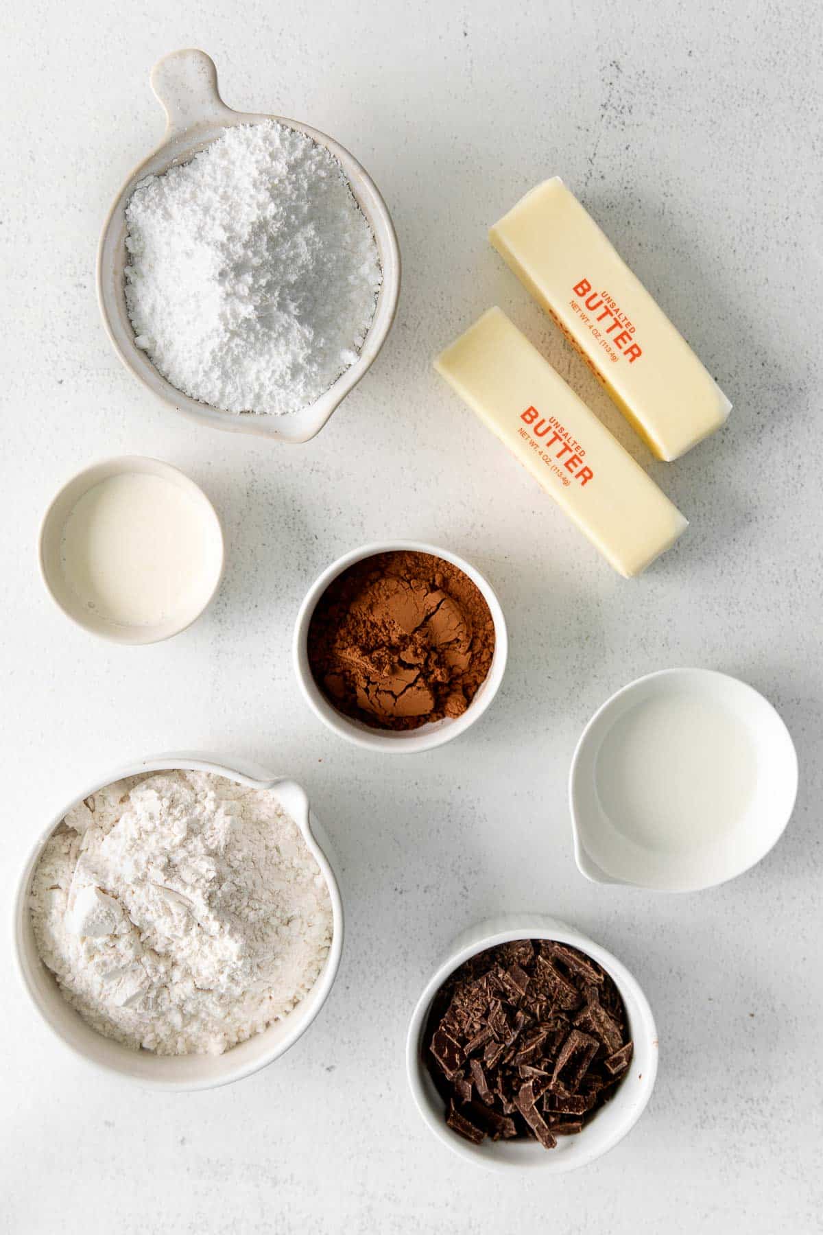 several small bowls with ingredients for chocolate cookies - flour, powdered sugar, cocoa powder, chocolate shavings, milk, two sticks of butter.