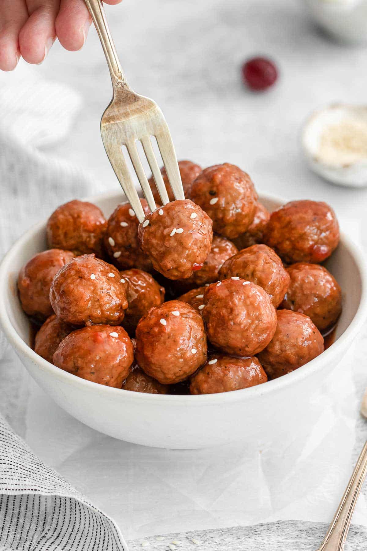 white bowl of meatballs in cranberry and sweet chili sauce with a fork picking up one.