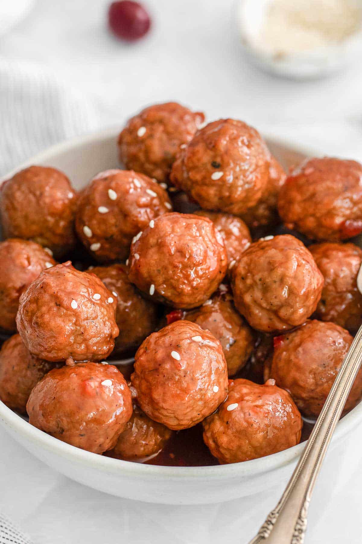 closeup of cranberry meatballs in a white bowl with a fork on the side.