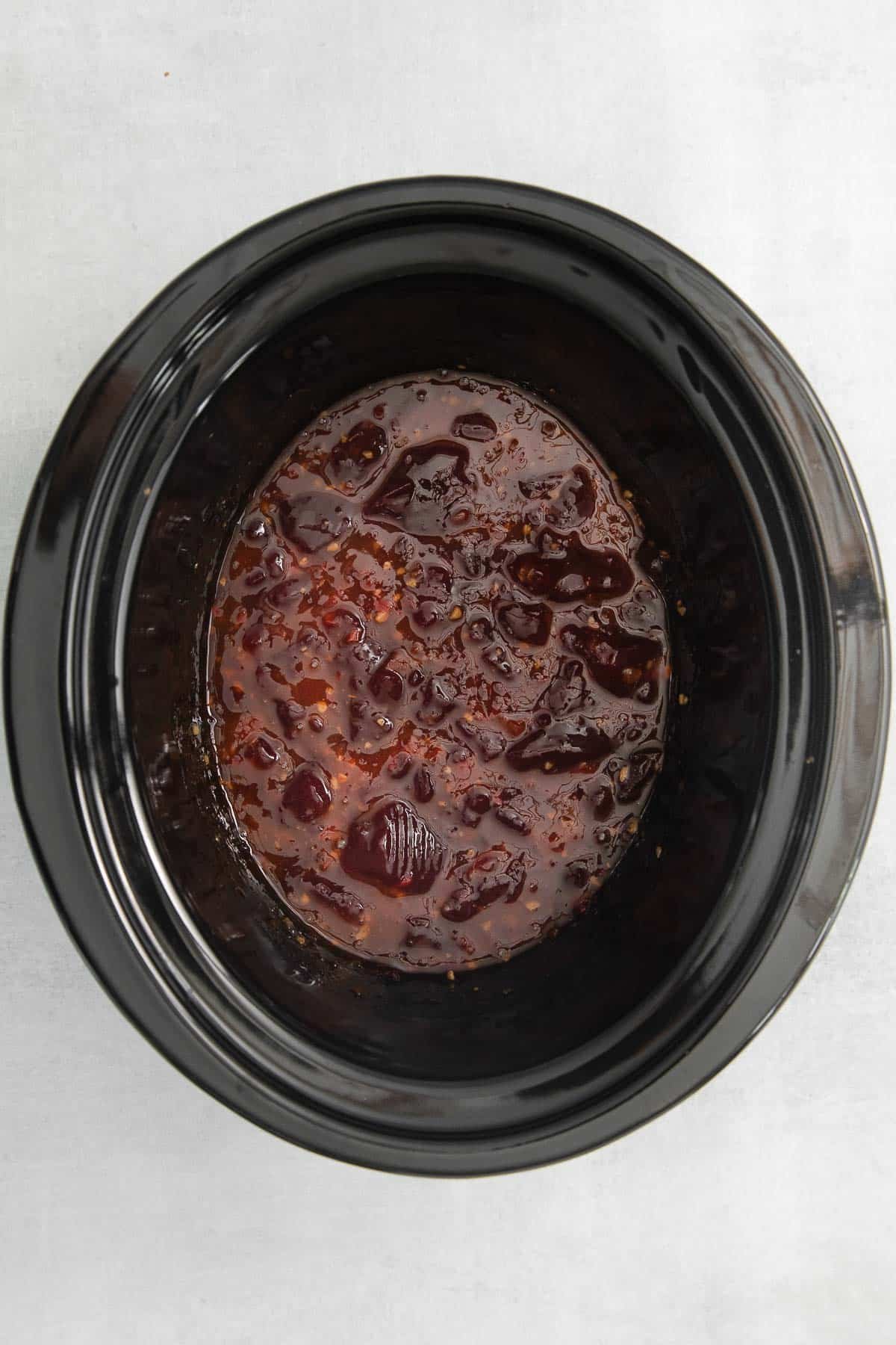 black slow cooker with cranberry sauce and chili sauce.