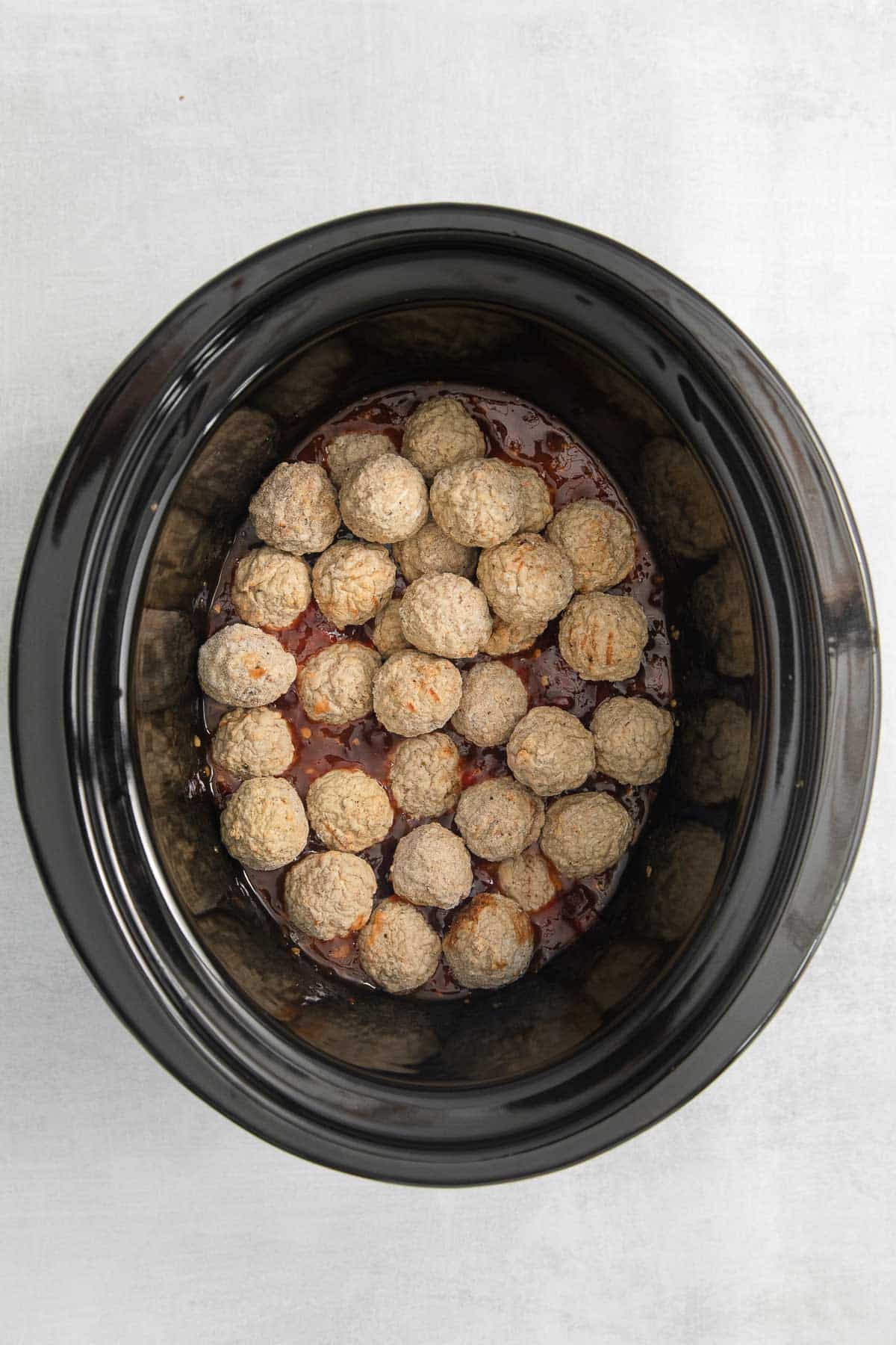 frozen meatballs in a black crock pot.