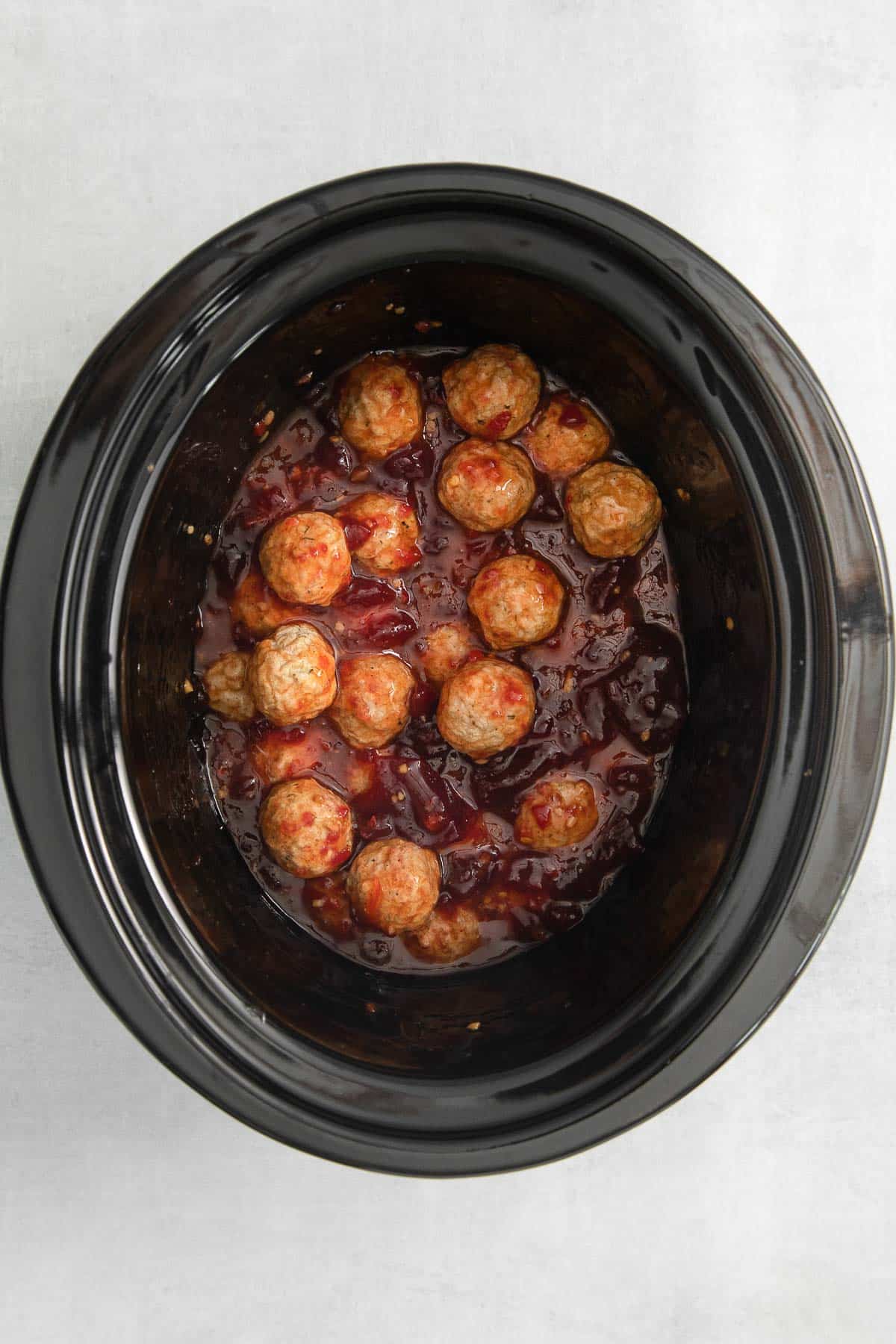 meatballs tossed in cranberry sauce mixture in a black crock pot.